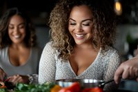 Young African American woman with curly hair smiling while cooking fresh vegetables in kitchen, wearing white sweater. Healthy lifestyle and home cooking concept.