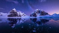 Majestic snow-capped mountain peaks reflecting in calm water under purple night sky with stars, creating mirror effect on glacial lake surface in winter landscape.