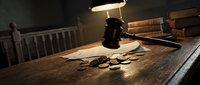 Wooden gavel and coins on rustic table under warm lamp light in courtroom setting. Legal justice concept for law firm presentations and financial litigation.