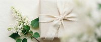 Elegant gift box wrapped in natural kraft paper with rustic twine bow, decorated with fresh white lilac flowers and green leaves for special occasions.
