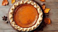 Fresh baked pumpkin pie with flaky crust and autumn leaves decoration on rustic wooden background, traditional Thanksgiving dessert served on table.