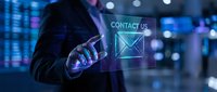 Professional businessman touching holographic contact us interface with email icon in modern digital office environment with blue lighting and data displays.