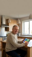 Senior Caucasian man using tablet computer in modern kitchen with wooden cabinets and pendant lights for smart home technology and digital lifestyle.