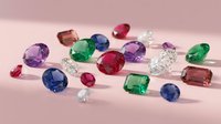 Collection of colorful precious gemstones including diamonds, emeralds, rubies and sapphires scattered on pink surface for jewelry design and luxury concepts.