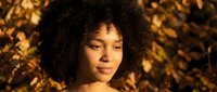 Young African American woman with natural curly hair enjoying warm golden sunlight outdoors during autumn season with bokeh background.