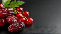 Fresh red dates and cranberries with green leaves on dark wooden background for healthy eating and natural nutrition concepts.