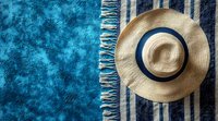 Straw sun hat with navy blue ribbon on striped beach towel against turquoise blue textured background, summer vacation concept for travel and leisure.