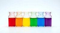 Colorful liquid samples in glass vials arranged in rainbow spectrum from red to purple on white background for laboratory research and chemical analysis.