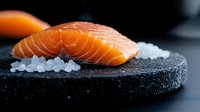 Fresh raw salmon fillet on black stone plate with sea salt crystals, dramatic lighting and dark background for restaurant menu and food photography.