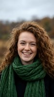 Happy young Caucasian woman with curly red hair wearing green knitted scarf smiling outdoors in autumn countryside setting for lifestyle photography.