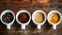 Coffee evolution shown in four white cups on rustic wooden background: whole beans, ground coffee, espresso, and cappuccino arranged in preparation sequence.