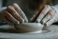Close-up of potter's hands shaping clay on spinning wheel, fingers covered in wet clay while crafting ceramic bowl in atmospheric lighting.