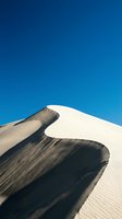 Contrasting sand dune with white and dark volcanic slopes against clear blue sky, showcasing natural desert landscape patterns and textures for travel and nature designs.