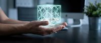 Young adult male hand holding glowing geometric holographic cube with lattice pattern on dark desk, representing technology, innovation, and digital transformation in modern workspace.