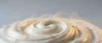 Creamy white swirl with golden highlights and flour dust particles creating dynamic motion against neutral background for culinary and baking projects.