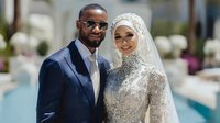 Elegant Muslim couple in formal wedding attire posing together outdoors. Groom in navy suit with sunglasses, bride in ornate hijab and embellished dress.