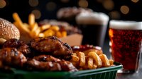 Grilled chicken wings with crispy french fries served in green basket, dark beer and soda drinks with bokeh lights background. Restaurant food setting.