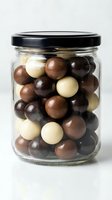 Mixed chocolate covered nuts in glass jar with black lid on white background for gourmet food packaging and confectionery marketing materials.