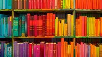 Colorful books arranged by spectrum colors on wooden library shelves creating vibrant rainbow pattern, educational and decorative background for reading concepts.