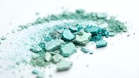 Crushed turquoise and mint green mineral powder with coarse granules scattered on white surface, suitable for cosmetics, art projects, and design backgrounds.