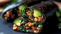 Fresh nori wrap filled with avocado, spicy chickpeas, greens and vegetables in black rice paper roll, close up view showing texture and layers. Plant based meal.