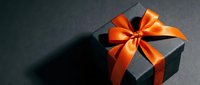 Black gift box with elegant orange satin ribbon bow on dark surface for holidays, birthdays, celebrations and special occasions.