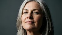 Senior woman with long gray hair and fair complexion, appearing thoughtful and serene against neutral background, suitable for healthcare, wellness, aging, and lifestyle editorial use.