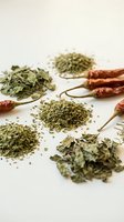 Dried herbs and red chili peppers scattered on white surface for culinary seasoning and cooking ingredients preparation.
