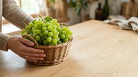 Green grapes in wicker basket held by person's hands on wooden table, fresh fruit harvest for food and nutrition concepts.