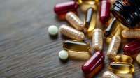 Colorful dietary supplements and vitamin pills scattered on dark wooden surface, including omega-3, fish oil capsules and round tablets. For health concepts.