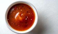 Vibrant red tomato soup with spices and herbs in white ceramic bowl on light background, top view angle showing texture and natural ingredients.