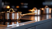 Stainless steel cooking pot on modern induction cooktop with warm lighting, showcasing contemporary kitchen interior and professional cookware setup.