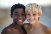 Two cheerful young boys, one African American with curly dark hair and one Caucasian with blonde hair, smiling together in close-up portrait showing friendship and diversity.