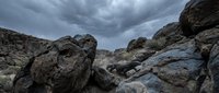 Dramatic rocky landscape with large boulders scattered across arid terrain under stormy cloudy sky, suitable for nature backgrounds and environmental design projects.