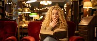 Young blonde woman reading book in cozy vintage library with warm lighting and red velvet armchairs. Perfect for education and leisure concepts.