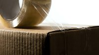 Clear adhesive tape on cardboard box roll, close-up macro shot showing transparent tape dispenser and brown packaging material for shipping, storage, and logistics applications.