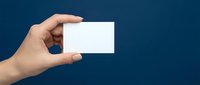 Female hand holding blank white business card on dark blue background, mockup with copy space for branding and design.