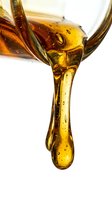 Golden oil pouring from bottle with droplet forming against white background, suitable for cooking, skincare, and wellness product marketing materials.