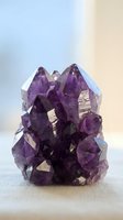 Amethyst crystal cluster with deep purple faceted points on a light surface, showcasing natural gemstone texture and sparkling mineral formation.