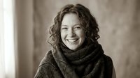 Happy middle-aged Caucasian woman with curly hair wearing cozy sweater smiling warmly in natural light for lifestyle and wellness concepts.
