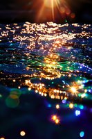 Magical water surface with sparkling light reflections creating ethereal bokeh effect in blue and golden colors. Dreamy abstract background for spiritual themes.