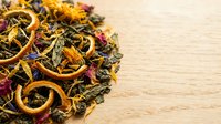 Dried herbal tea blend with orange slices, flowers and botanicals on wooden surface for wellness and beverage design projects.