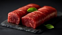 Fresh raw beef tenderloin steaks on black stone board with green basil leaves, dramatic dark background with selective focus for restaurant menu.