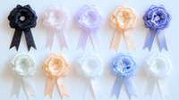 Delicate fabric rosettes with flowing ribbons in pastel and dark colors arranged on white background, isolated decorative elements for crafting and celebrations.