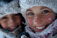 Close up portrait of smiling faces with rosy cheeks covered in snow and frost during winter outdoor activities, expressing joy and seasonal fun in cold weather.
