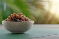 Sweet golden raisins in ceramic bowl on turquoise surface against blurred green background with sunlight, healthy dried fruit snack for natural eating.