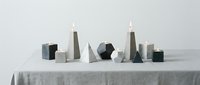 Modern geometric candle holders in various shapes including hexagon, triangle, and cube forms arranged on white linen tablecloth for minimalist home decor styling.