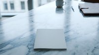 Closed silver laptop computer on elegant marble desk surface in modern office workspace with natural lighting and urban building view through window.