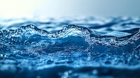 Close-up macro shot of ocean wave surface with crystal clear water texture showing ripples, splashes and dynamic movement in deep blue tones. Natural background.