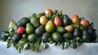 Fresh avocados and apples arranged on green leaves against neutral background, creating natural composition for food photography and healthy lifestyle content.